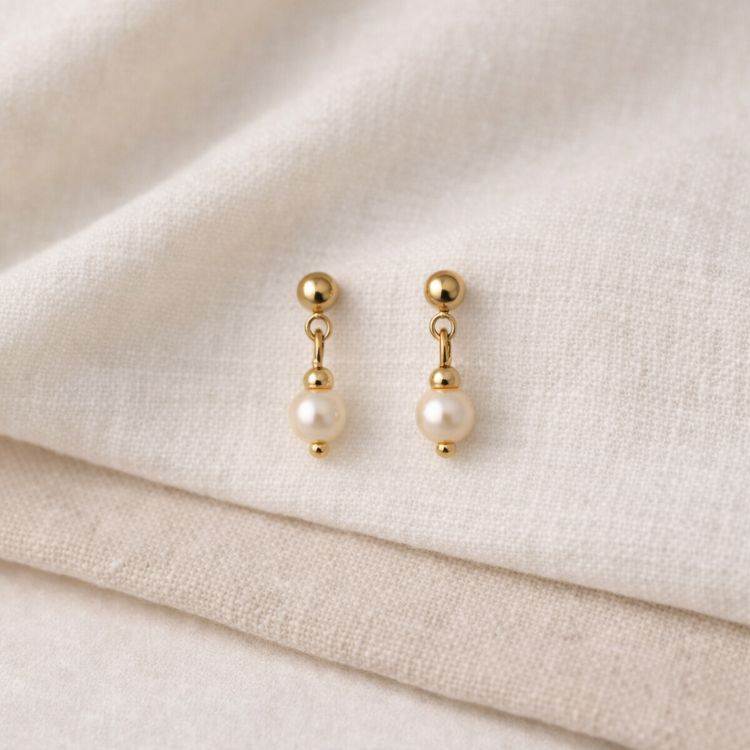 Aretes de perla crema pequeños en composición minimalista