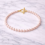 Pulsera de perla rosa pastel pequeña sobre mármol