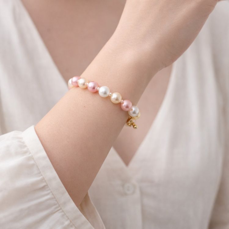 Mujer usando pulsera de perlas en tonos blanco crema y rosa
